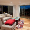 A lounge room, featuring wooden floor boards and large windows.
